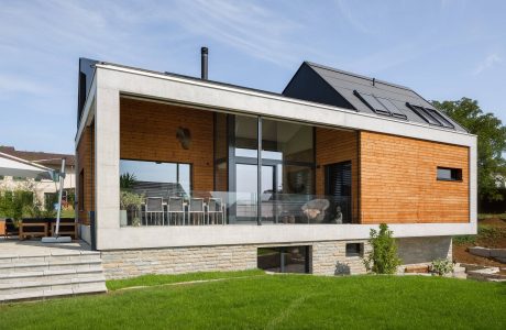 A modern, minimalist house with large windows, wooden panels, and a spacious terrace.