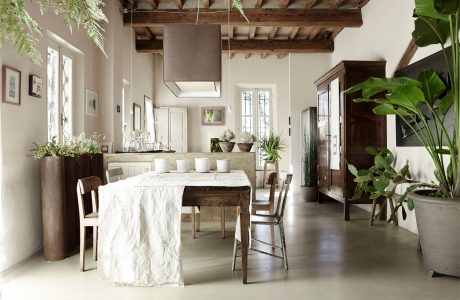 Rustic dining room with exposed wooden beams, linen-draped table, and lush greenery.