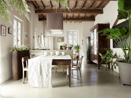 Rustic dining room with exposed wooden beams, linen-draped table, and lush greenery.