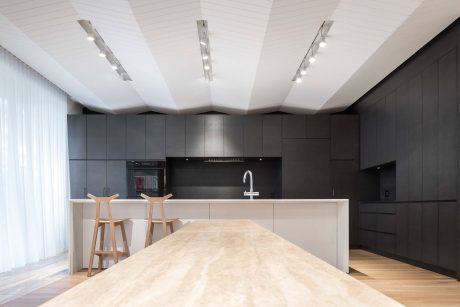 Sleek, modern kitchen with minimalist black cabinetry, white countertops, and track lighting.