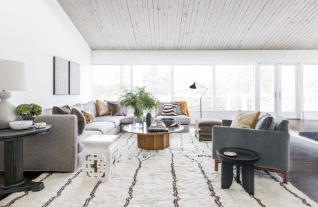 Spacious living room with wood-paneled ceilings, large windows, and a plush, patterned rug.