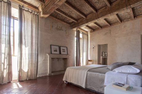 A rustic bedroom with a high wooden ceiling, textured walls, and curtained windows.