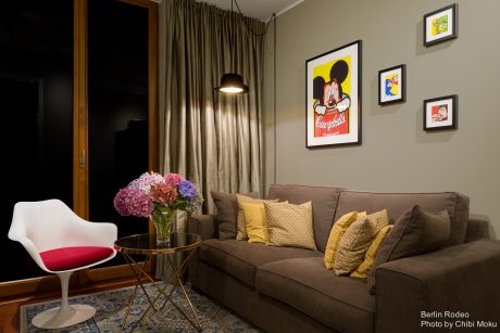 A cozy living room with a plush brown sofa, colorful artwork, and a bold light fixture creating a warm, inviting atmosphere.