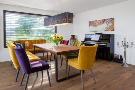 Vibrant, modern dining room with floor-to-ceiling windows, wooden table, and colorful furniture.