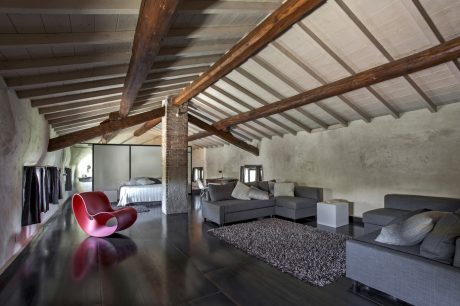 Rustic loft-style room with wooden beams, gray sofas, and a bold red chair.
