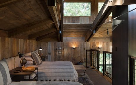 Rustic cabin bedroom with wooden walls, high ceiling, and cozy furnishings.