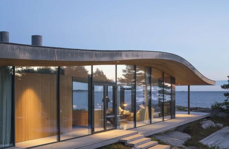 A modern, curved lakeside retreat with large glass windows and a wood-paneled exterior.