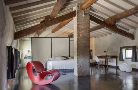 A cozy attic space with exposed wooden beams, brick columns, and a modern red rocking chair.