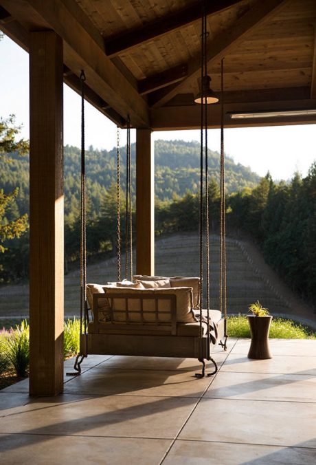 Rustic wooden porch with hanging swing and views of lush forested landscape.
