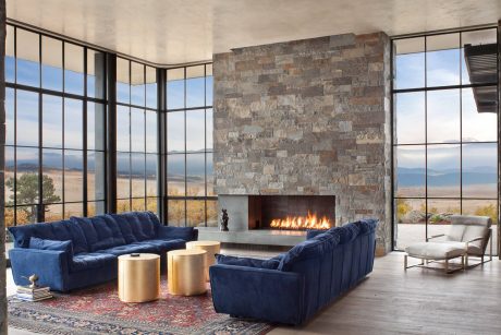 Spacious modern living room with floor-to-ceiling windows, stone fireplace, and plush navy sofas.