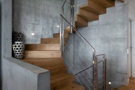 Minimalist staircase with concrete walls, wooden treads, and metal railing.