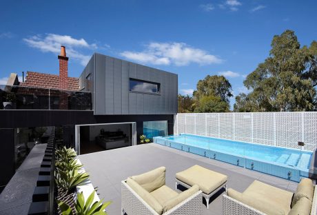 A sleek, contemporary home with a pool, surrounded by lush greenery and a white fence.