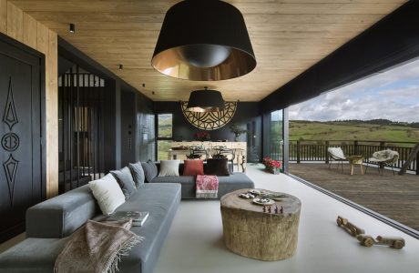 Rustic-modern living room with wooden ceiling, black pendant lamps, and scenic outdoor view.