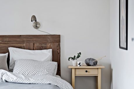 Rustic wood headboard, minimalist bedside table, small potted plant, and cozy bedding.
