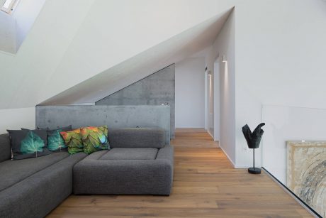 Minimalist interior design with angled walls, hardwood floors, and cozy gray sectional.