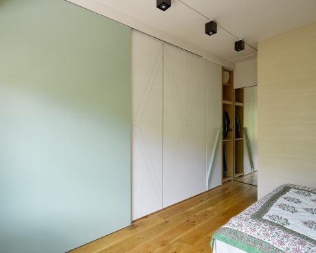 Modern bedroom with minimalist white closet doors, hardwood flooring, and recessed lighting.