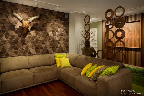 A modern living room with a patterned feature wall, wooden decor, and a plush brown sectional.