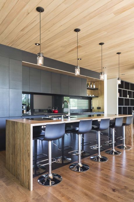 A modern kitchen with dark cabinets, wooden ceiling, and pendant lighting over a central island.