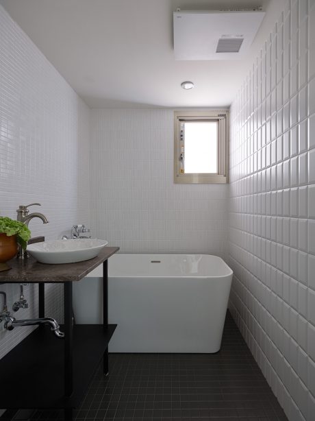 Minimalist bathroom interior with square ceramic tiles, freestanding tub, and vessel sink.