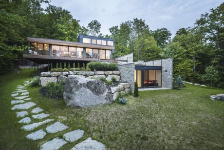 A modern, minimalist home nestled in a lush, forested landscape with a natural stone exterior.