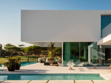 A modern, minimalist villa with a pool, surrounded by lush greenery and a sleek, cantilevered roof.