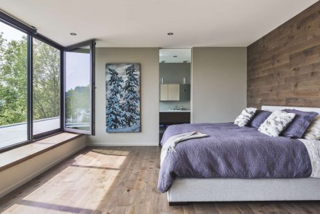 Spacious bedroom with wooden accent walls, large windows, and modern furnishings.