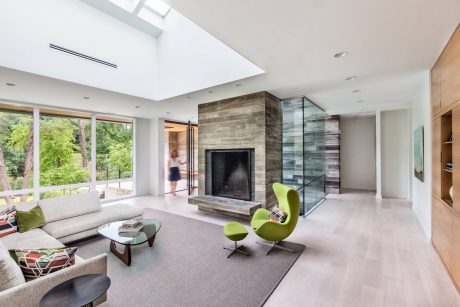 Spacious living room with glass walls, stone fireplace, and modern green chairs.