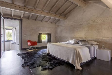 Rustic bedroom with exposed wooden beams, stone walls, and minimalist furnishings.