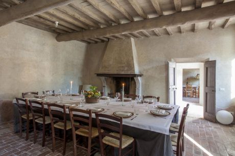 Rustic dining room with exposed wooden ceiling beams, stone fireplace, and wooden furniture.