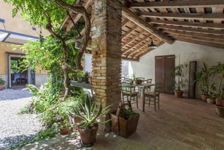 Charming rustic patio with brick arches, wooden beams, and lush potted plants.