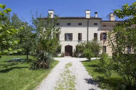 Charming Italian villa with ornate arched entryway, surrounded by lush greenery.