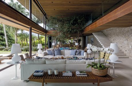 Spacious living area with wooden beams, stone walls, and lush greenery outside.