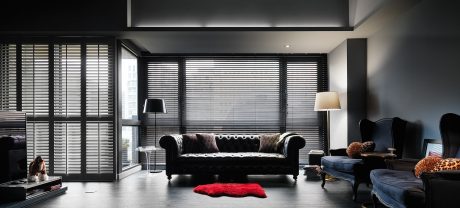 Luxurious living room with sleek black furniture, floor-to-ceiling shutters, and a plush red rug.