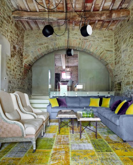 Rustic stone arch frames living space with modern gray sofa, bright accents.