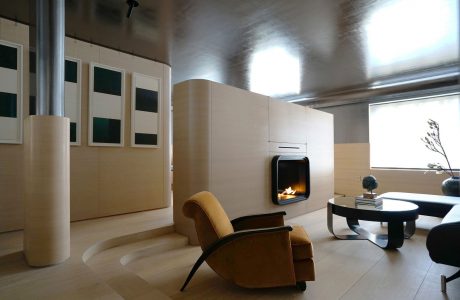 Spacious, minimalist living room with wood-paneled walls, a fireplace, and sleek, modern furniture.