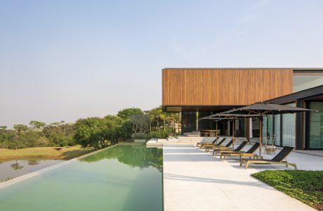 Sleek modern wooden exterior, inviting pool, and lounging area overlooking lush greenery.