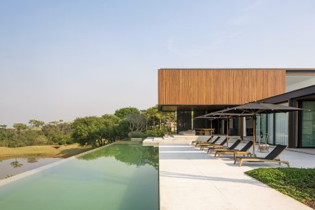 Sleek modern wooden exterior, inviting pool, and lounging area overlooking lush greenery.