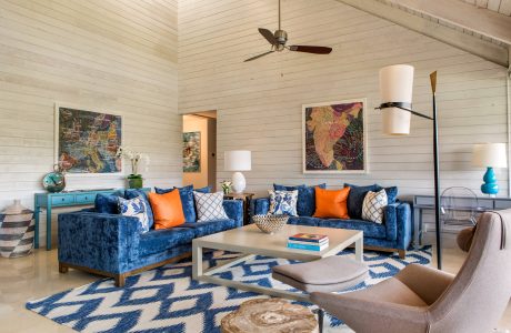 A cozy living room with a distinctive blue velvet sofa, vibrant artwork, and intricate patterned rug.