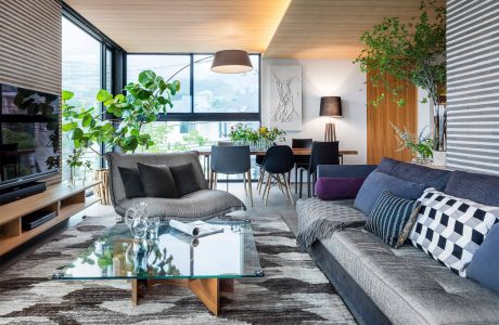 Airy, modern living space with lush greenery, glass coffee table, and eclectic decor.