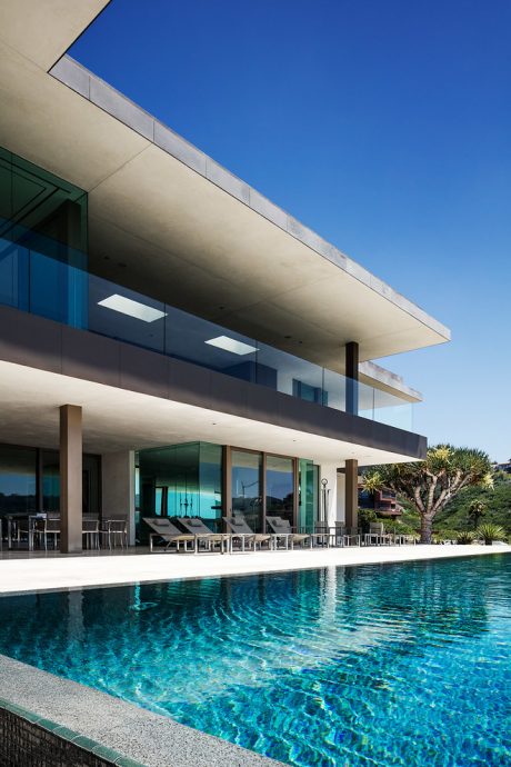 A modern, minimalist house with a sleek, cantilever roof, glass walls, and a sparkling pool.