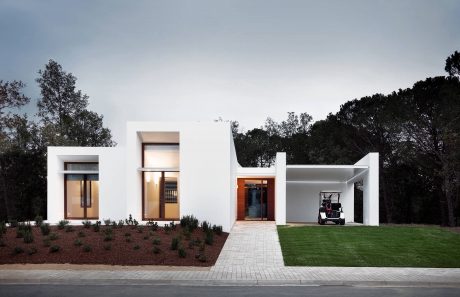 A modern, minimalist, single-story home with a clean, geometric facade and landscaped yard.