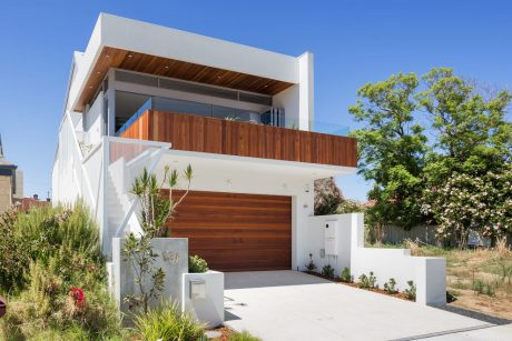 Modern two-story house with wooden accents, glass walls, and a lush garden.