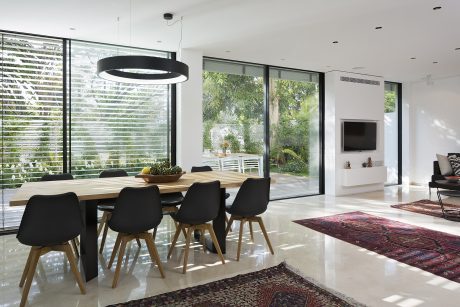 Modern, open-plan dining area with large windows overlooking lush greenery, sleek black chairs, and wooden dining table.