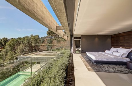 Expansive modern bedroom with floor-to-ceiling glass walls overlooking verdant landscape.