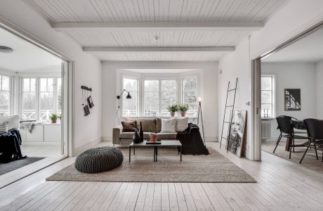 Cozy and modern living room with white wood ceiling, large windows, and neutral furnishings.