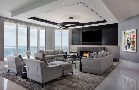 Expansive living room with sleek modern furnishings, large windows, and a dramatic circular light fixture.