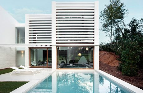 A modern house with a minimalist white facade, floor-to-ceiling windows, and a serene swimming pool.