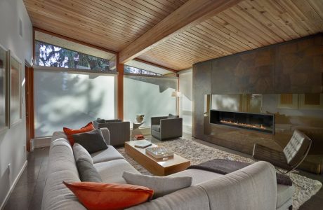 A spacious living room with a cozy fireplace, large windows, and a wooden ceiling.