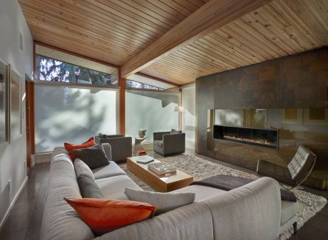 A spacious living room with a cozy fireplace, large windows, and a wooden ceiling.