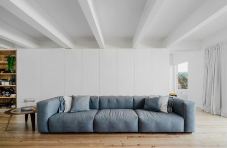 Large, plush gray sofa set against a white wall with high ceilings and wooden floors.